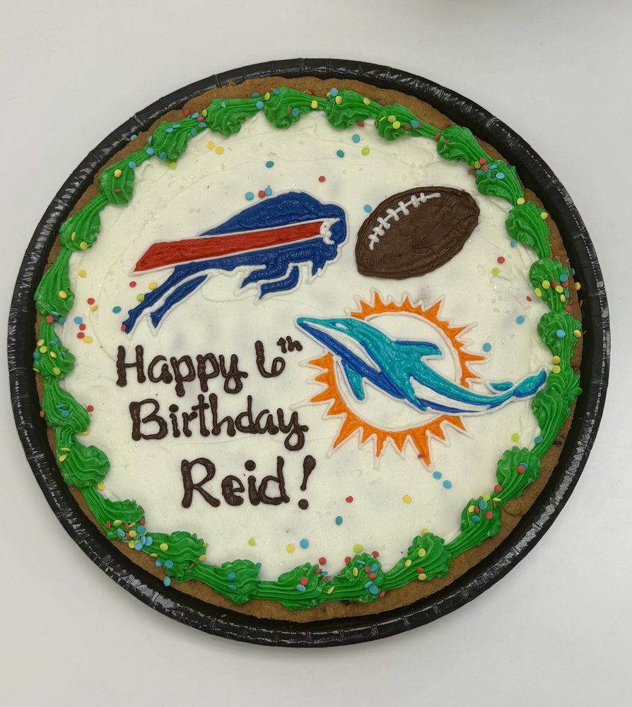 A birthday cookie cake iced with two football team helmets and a green piped border
