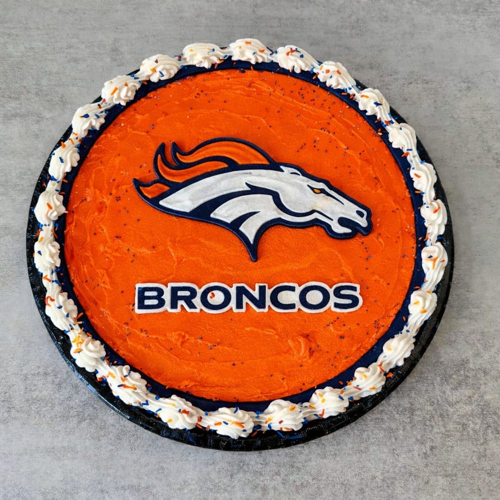 A cookie cake iced with a football team crest on orange, with a white piped border