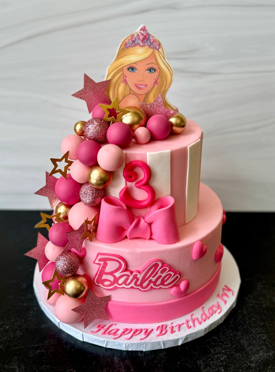 A pink tiered birthday cake with a doll topper