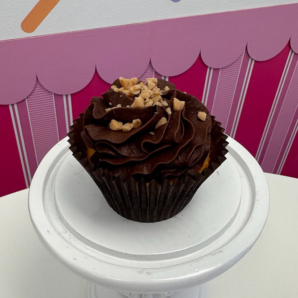 A cupcake with chocolate frosting, chopped nuts and a candy piece