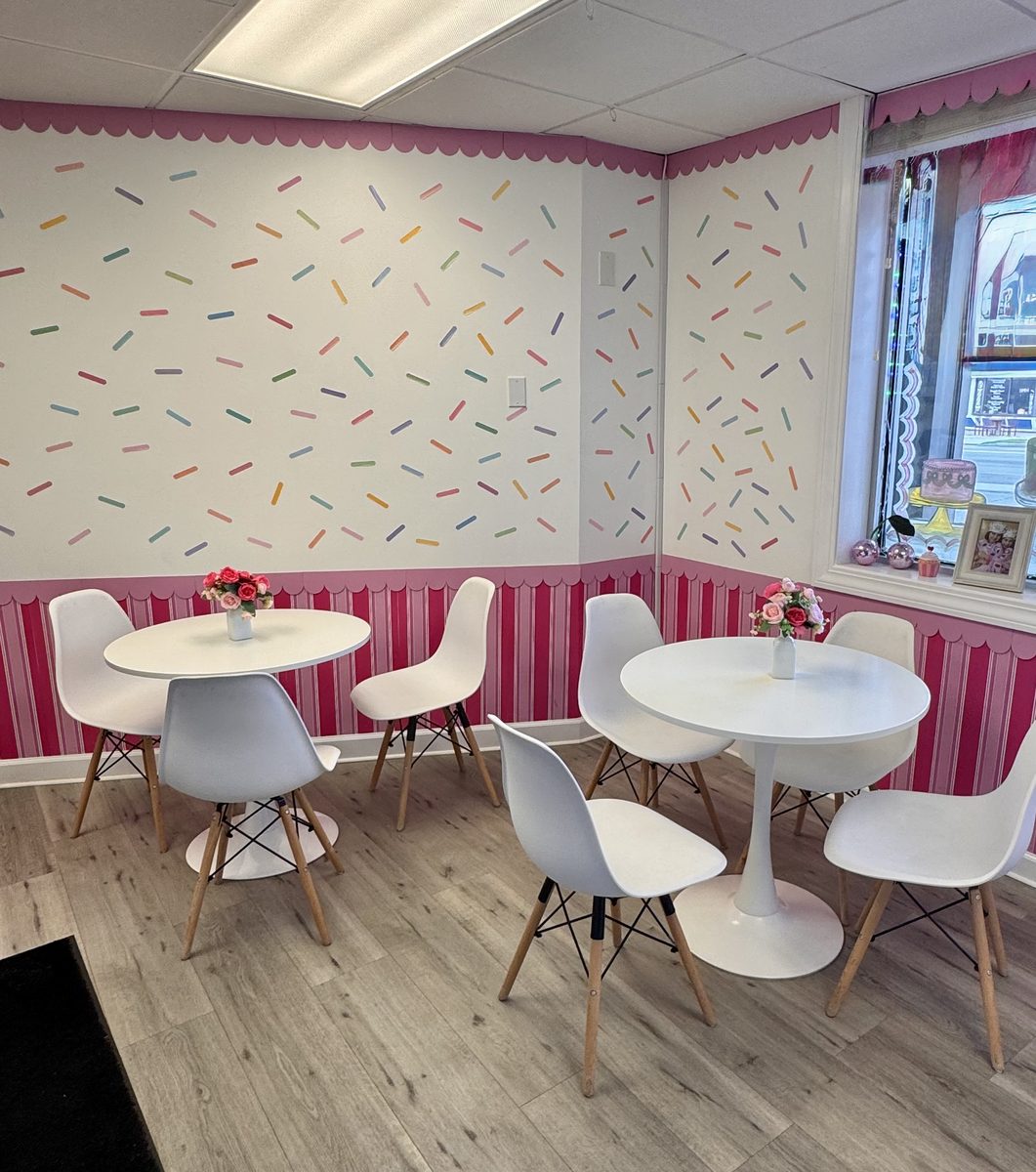 Round white tables and chairs under the sprinkle wall and pink stripes inside Mrs. Kelder's Cakes