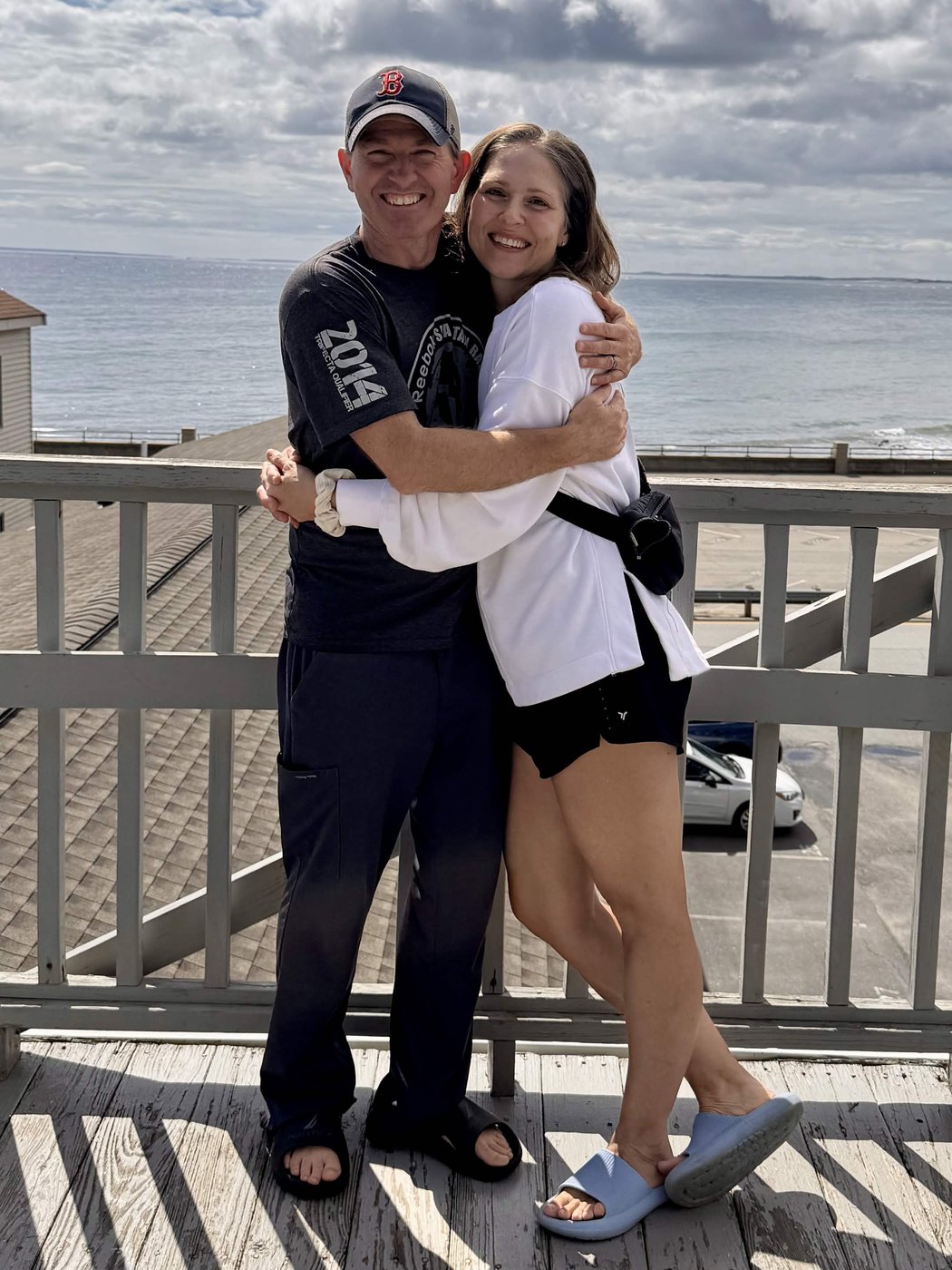 Derek and Cyndi Kelder hugging on a boardwalk deck above the beach