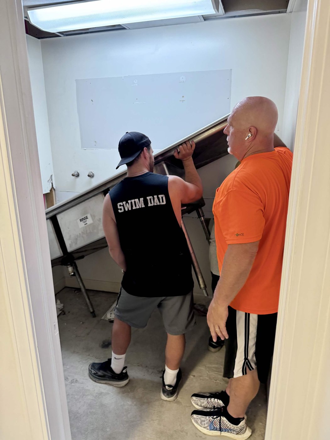 Two helpers tipping a stainless steel prep table through a doorway on moving day