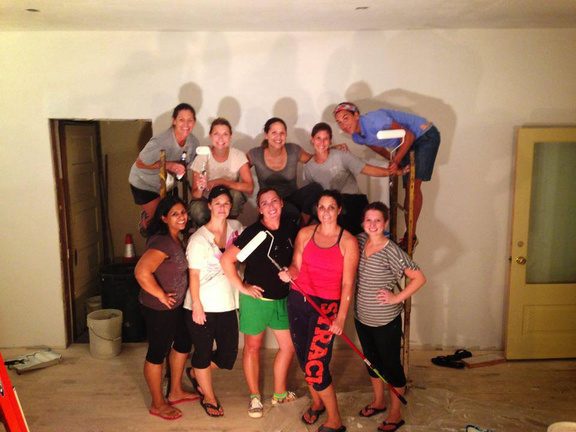 A crew of friends and family, paint rollers in hand, in the empty shop before it opened