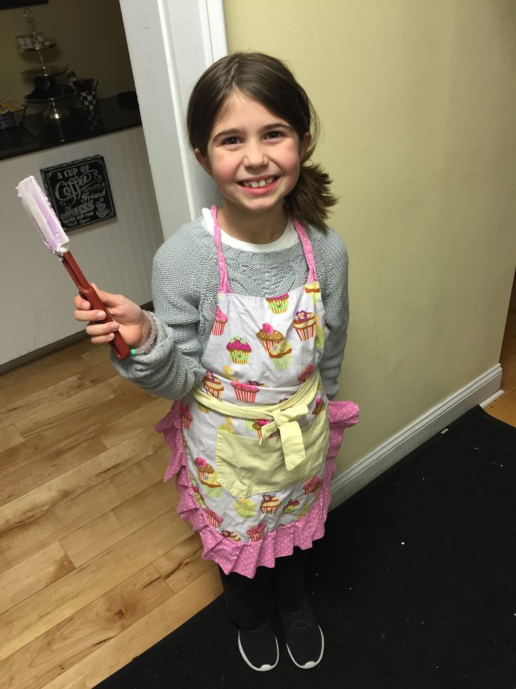 A young baker in a cupcake apron holding a spatula