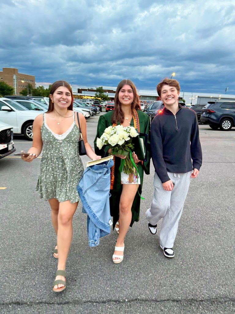 Three teenagers walking together, one carrying a bouquet of graduation flowers